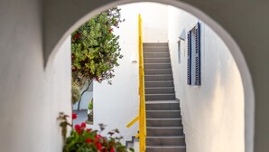 Una escalera conduce a un edificio blanco con contraventanas azules, enmarcado por un arco blanco.
