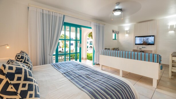 Habitación de hotel con cama, televisor, banqueta y vista al exterior.