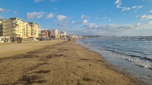 A beach with buildings along the shore, a clear sky, and waves approaching the beach. - Sea View Holiday Apartment 073 (Durres)