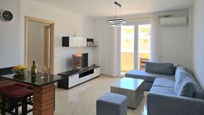 A modern living room with a sofa, ottoman, TV, and a dining area with a table and chairs. - Sea View Holiday Apartment 073 (Durres)