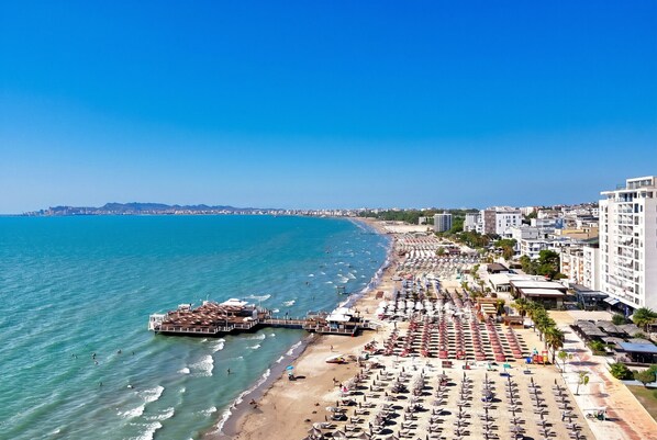 Un paisaje urbano costero con una playa, un muelle y una hilera de edificios frente al mar.