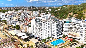 Ein Hochhaus-Hotel mit mehreren Etagen, einem Swimmingpool und einem Strandbereich mit Sonnenschirmen.