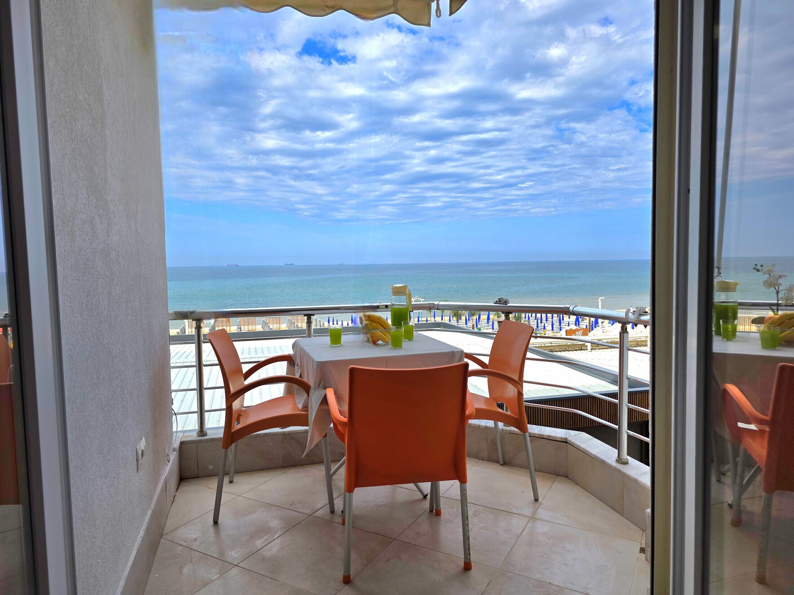 Ein Balkon mit Tisch und Stühlen mit Blick auf einen Strand und einen klaren Himmel.