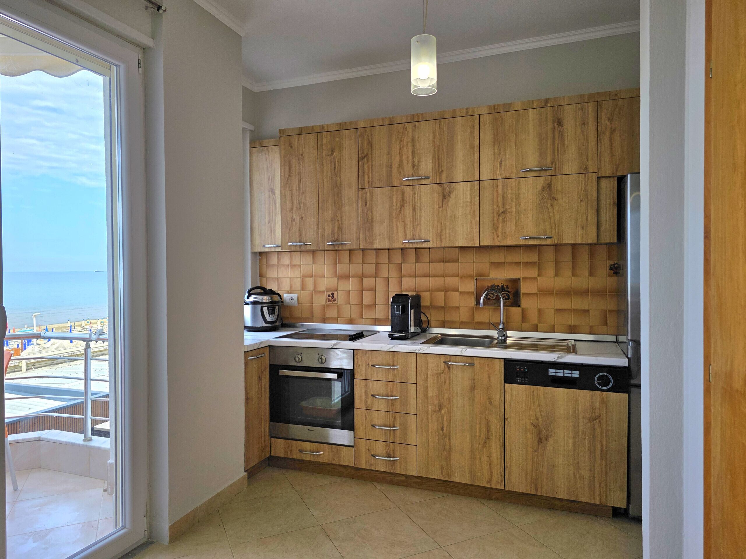 Eine moderne Küche mit Holzschränken, Backofen, Geschirrspüler und einem Fenster mit Meerblick.