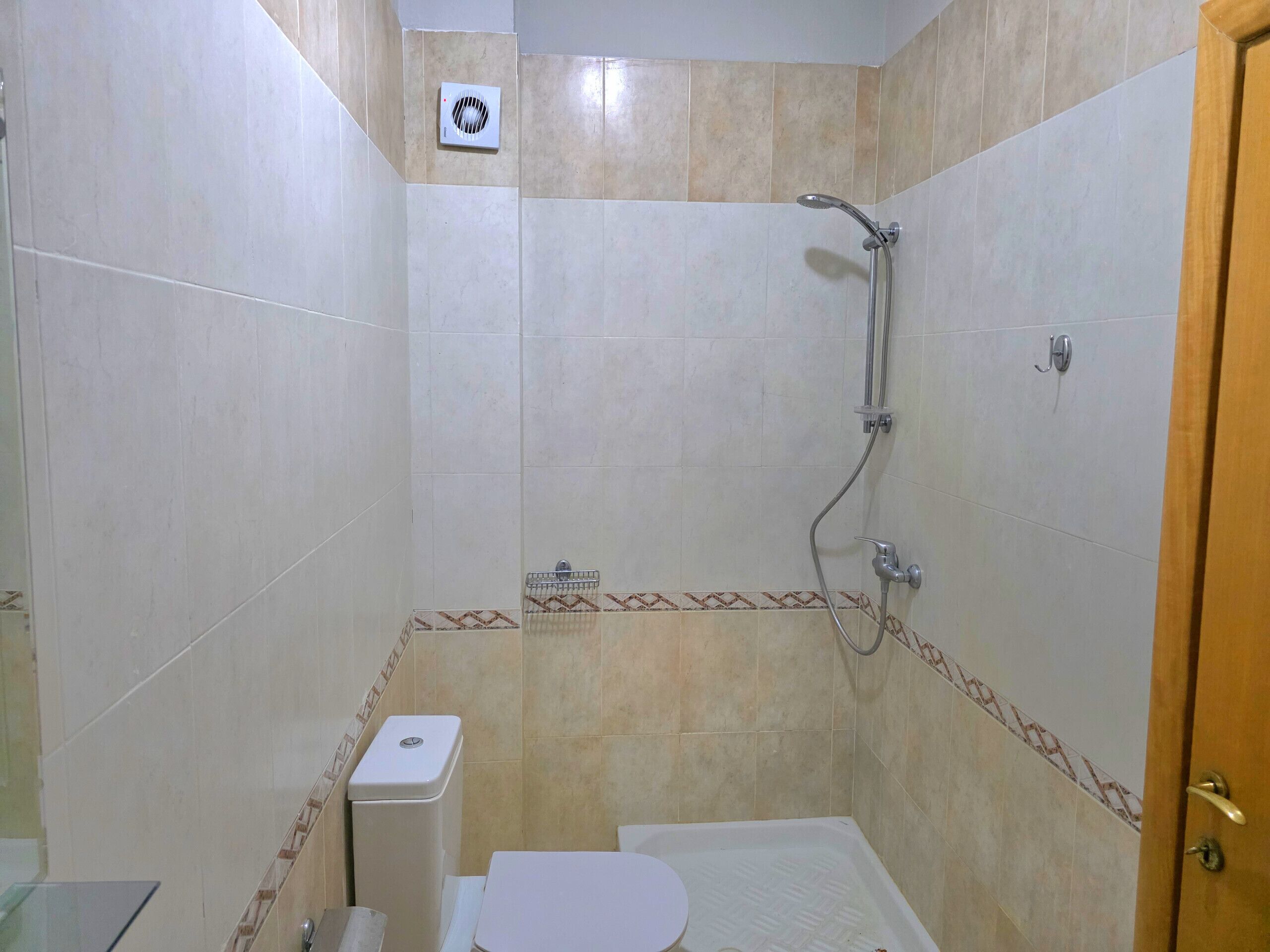 Ein kleines Badezimmer mit Fliesen, einer Dusche, einer Toilette und einem Mülleimer.