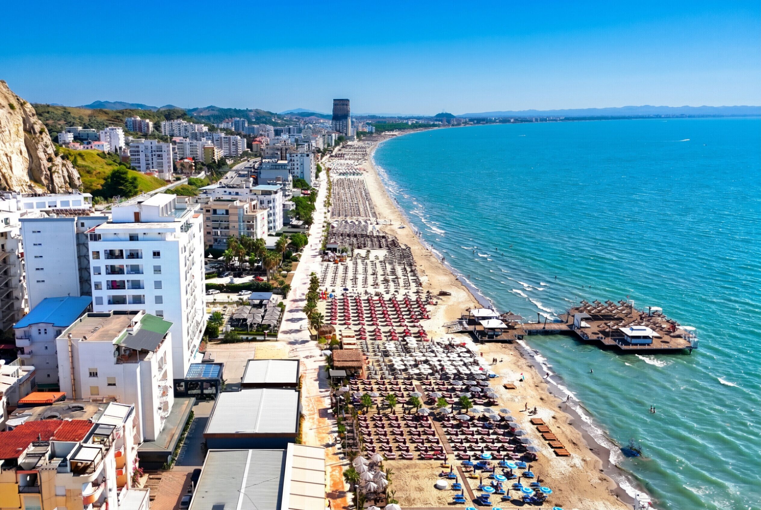 A coastal cityscape with a beach, buildings, and a clear sky.
