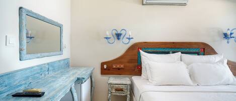 A bedroom with a wooden headboard, white bedding, a small bedside table, a mirror, and an air conditioning unit.
