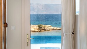 A room with a bed, a door leading to a balcony with a view of the sea, and a white curtain. - Deniz Evi (Cesme)