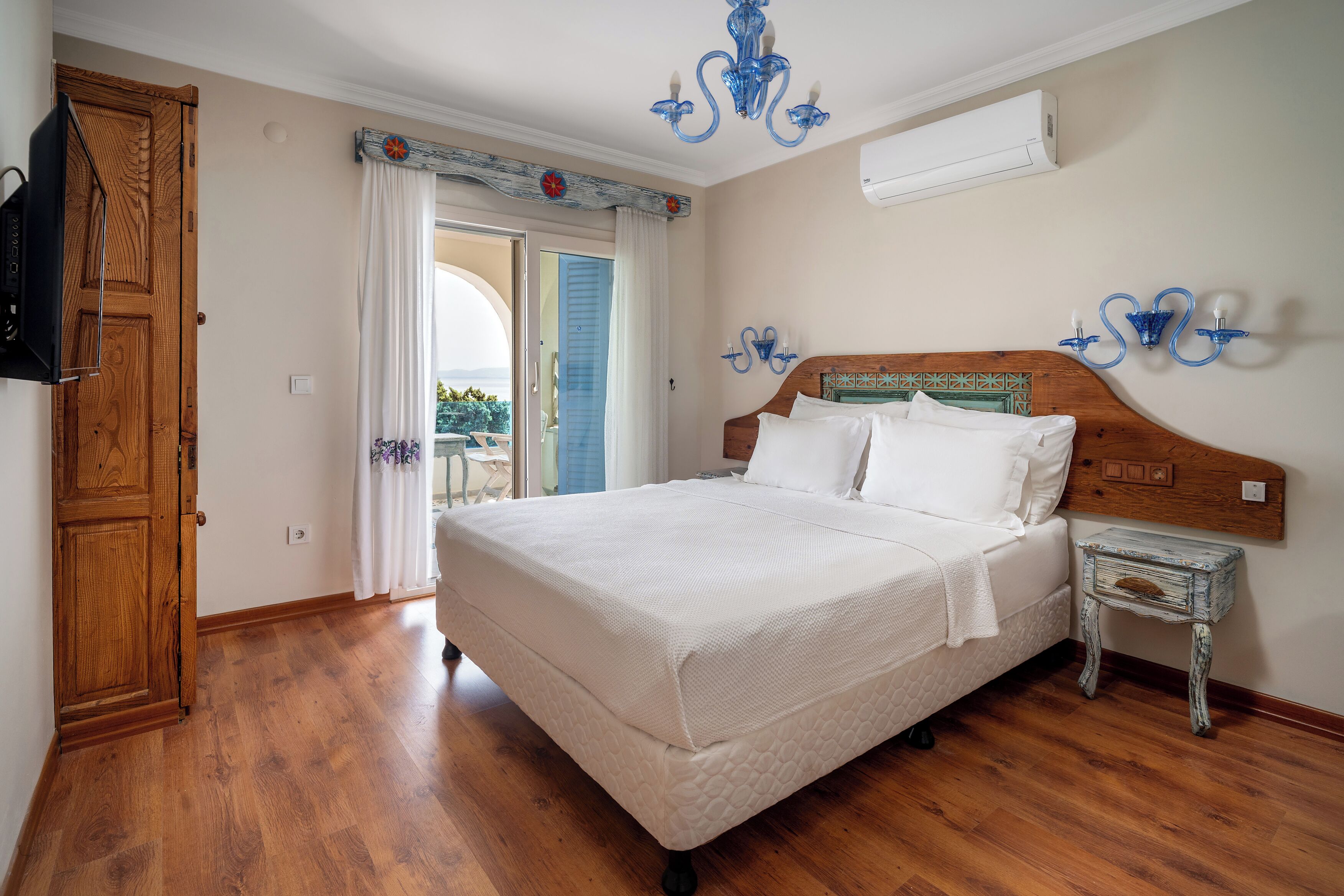 A bedroom with a wooden floor, a bed with white bedding, a wooden nightstand, and a blue wall-mounted light fixture.