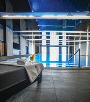 Habitación de hotel con cama, un vaso de bebida y vista a una piscina cubierta.