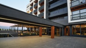 Un hôtel moderne à plusieurs étages, doté d’un espace extérieur couvert avec des sièges et offrant une vue sur les montagnes.