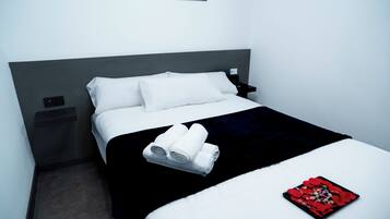 Una cama bien hecha con sábanas blancas, una colcha negra y una almohada decorativa roja.