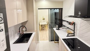 Une cuisine moderne avec des meubles blancs, une cuisinière noire et une porte en verre donnant sur un coin repas.