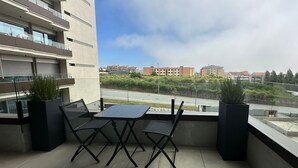 Un balcon avec une table et des chaises, des plantes en pot et une vue sur les bâtiments et la verdure.