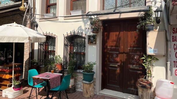 An outdoor seating area with a table and chairs, surrounded by potted plants and a wooden door.
