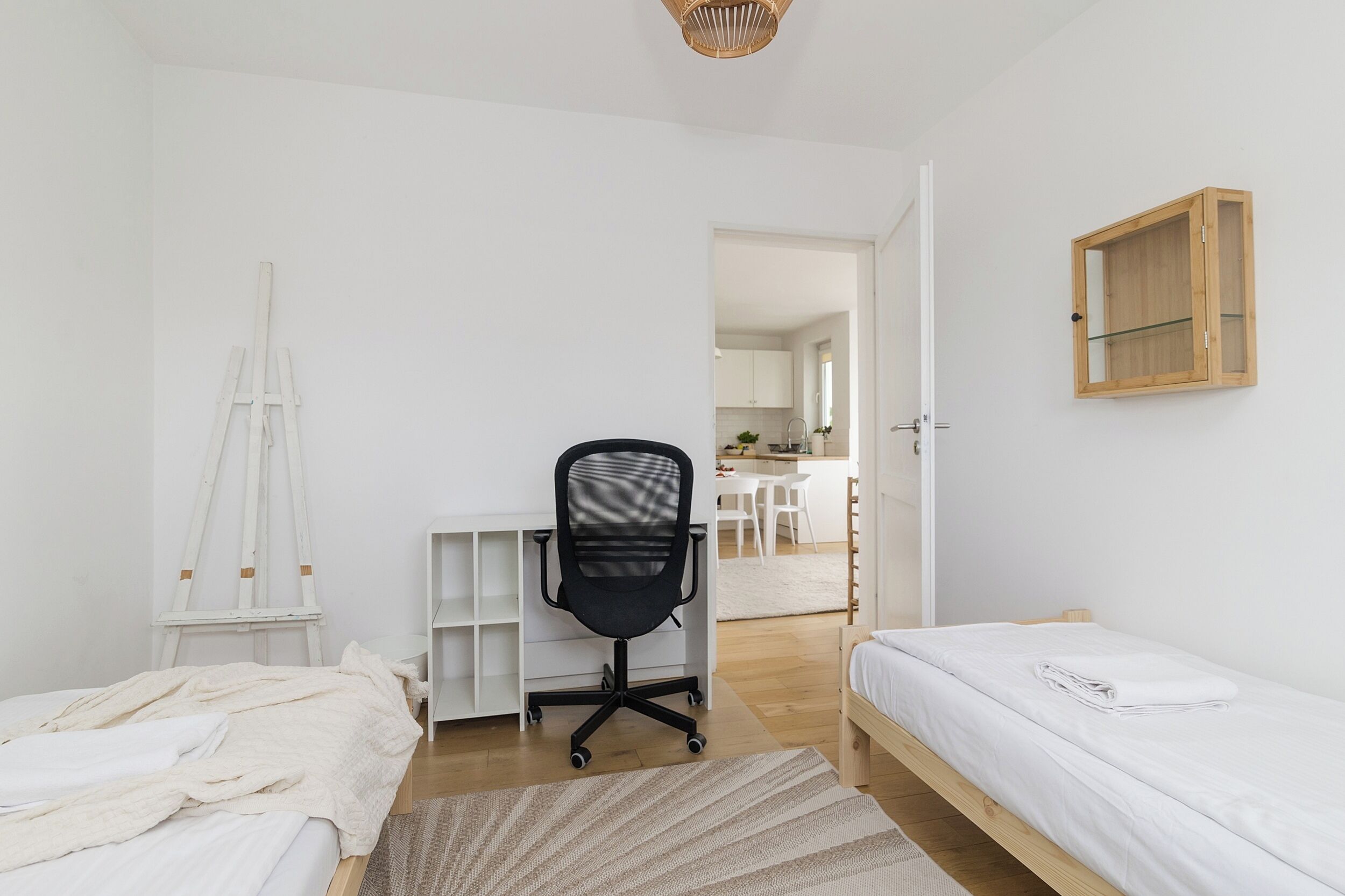 A bedroom with a bed, a desk, and a chair. There is a wooden cabinet on the wall and a door leading to another room.