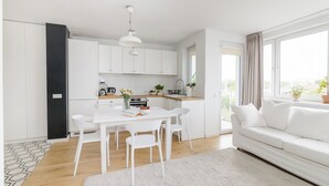 Une cuisine moderne avec des meubles blancs, une table à manger avec des chaises et un canapé blanc dans un salon lumineux doté de grandes fenêtres.