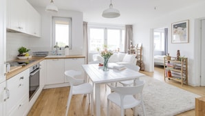 Une cuisine moderne avec des meubles blancs, un plan de travail en bois et un coin repas comprenant une table et des chaises blanches.