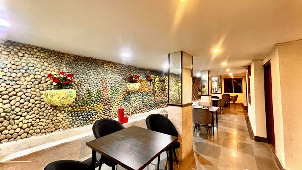 A dining area with a stone wall, a table with chairs, and a hallway leading to another room. - Hotel Roshie Mall Road Mussoorie  (Mussoorie)