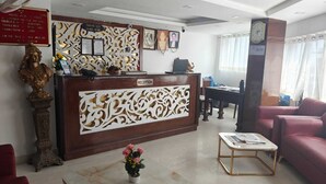 A hotel reception area with a reception desk, a three-seater sofa, a coffee table, and a decorative bust. - Hotel Roshie Mall Road Mussoorie  (Mussoorie)