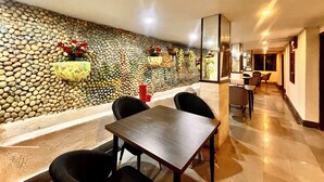 A dining area with a stone wall, a wooden table, and black chairs. - Hotel Roshie Mall Road Mussoorie  (Mussoorie)