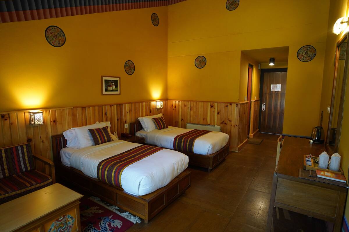 Habitación de hotel con dos camas, cabeceros de madera y un pequeño escritorio con espejo.