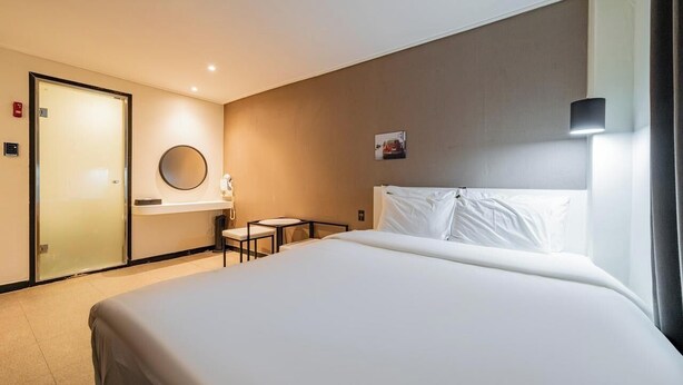 Een hotelkamer met een groot bed, een bureau, een stoel, een ronde spiegel en een deur.