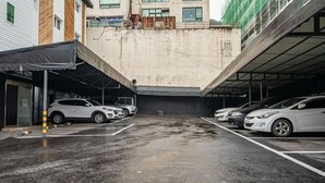 Een parkeerplaats met meerdere auto's, een overdekte ingang en een gebouw met een betonnen gevel.