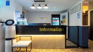 Een hotel receptie met een marmeren wand, een receptiebalie met de tekst 'Informatie', een digitaal scherm en een waterkraan.