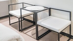 Twee zwarte metalen stoelen met witte kussens in een kamer met een witte muur en een raam.
