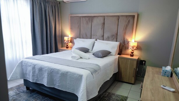 Een hotelkamer met een groot bed, twee nachtkastjes met lampen, een houten hoofdbord en een klein bureau met een afstandsbediening.