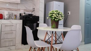Een moderne keuken met witte kasten, een zwart fornuis en een witte koelkast. Er staat een eettafel met witte stoelen en een potplant.