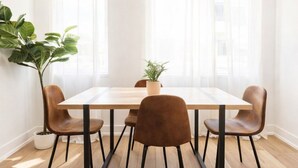 A dining area with a wooden table and four brown chairs, a potted plant, and large windows with sheer curtains. - ReeseStreetUnit2inPhilly. (Philadelphia)