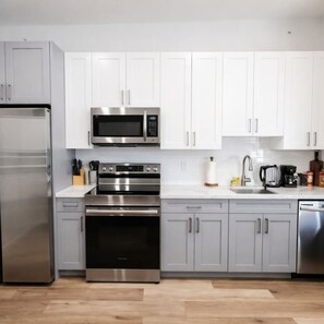 Una cucina moderna con elettrodomestici in acciaio inossidabile, mobili bianchi e pavimento in legno.