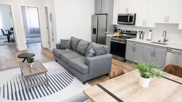 A modern apartment with a grey sofa, a wooden dining table, and a kitchen area with white cabinets and appliances. - ReeseStreetUnit2inPhilly. (Philadelphia)