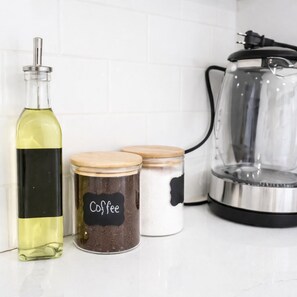 Un piano di lavoro in cucina con una bottiglia d'olio d'oliva, due barattoli con l'etichetta 'Caffè' e una macchina da caffè.