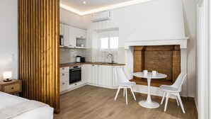 A compact kitchen with white cabinets, a built-in oven, and a brick fireplace. There is a dining area with two white chairs and a small round table. - Casa Milonopoulos by Konnect, Studio & Main House (Corfu)