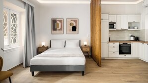 A modern bedroom with a large bed, bedside tables, and a view into a kitchen area. - Casa Milonopoulos by Konnect, Studio & Main House (Corfu)