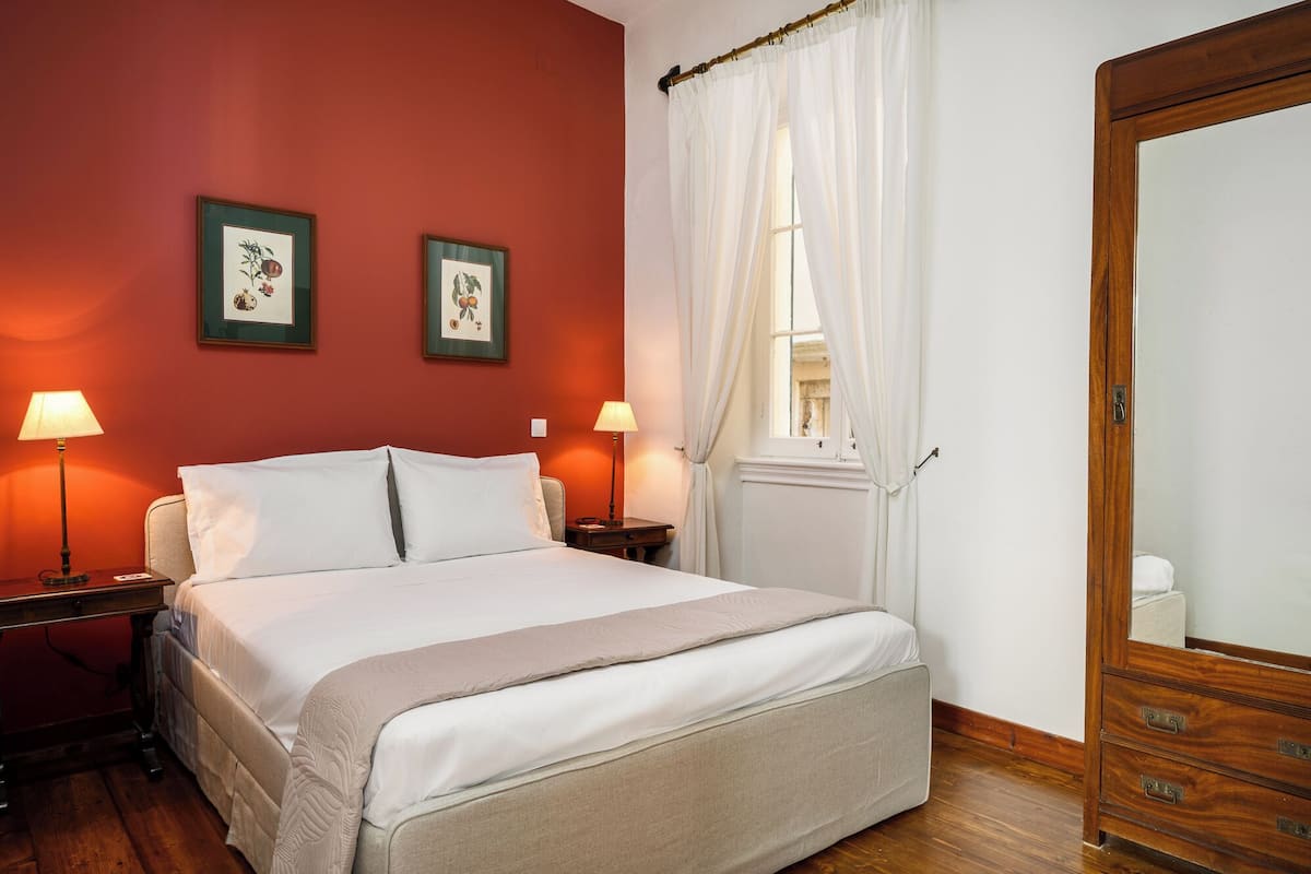 Ein Hotelzimmer mit einem Bett, zwei Nachttischlampen, einer Holzkommode, einem Spiegel und zwei gerahmten Pflanzenbildern an der Wand.