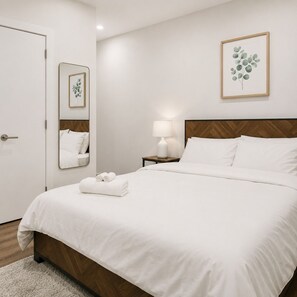 Un letto rifatto con lenzuola bianche, un comodino con una lampada, uno specchio e una stampa botanica incorniciata appesa al muro.