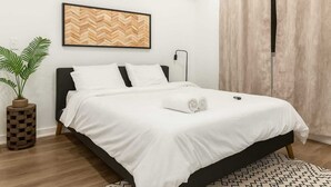 A neatly made bed with white linens, a wooden headboard, and a small bedside table with a plant. - Stylish 2BR/2BA near TempleU with Wi-Fi, in-unit laundry & parking (Philadelphia)