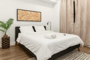 Un letto rifatto con lenzuola bianche, una testiera in legno e un comodino con una pianta.