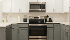 A modern kitchen with white cabinets, stainless steel appliances, and a wooden floor. - Stylish 2BR/2BA near TempleU with Wi-Fi, in-unit laundry & parking (Philadelphia)