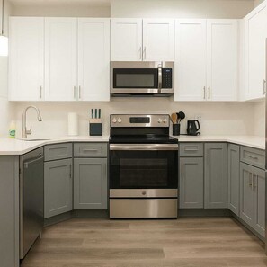 Una cucina moderna con mobili bianchi, elettrodomestici in acciaio inossidabile e pavimento in legno.