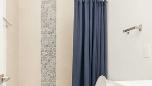 A bathroom with a white toilet, a bathtub, and a shower area with a mosaic tile wall. - Stylish 2BR/2BA near TempleU with Wi-Fi, in-unit laundry & parking (Philadelphia)