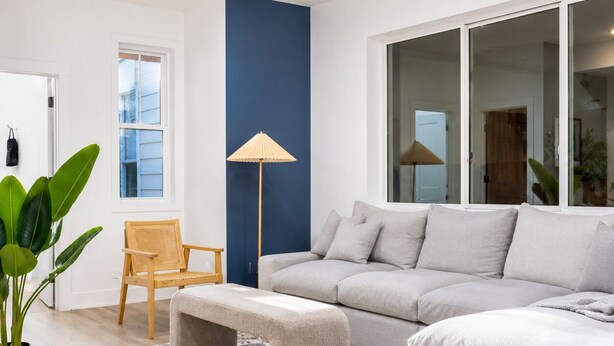 En moderne stue med sofa, bænk, stol, gulvlampe og en potteplante.