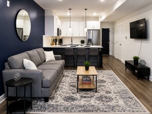 A modern living room with a sofa, a coffee table, a rug, and a TV mounted on the wall.