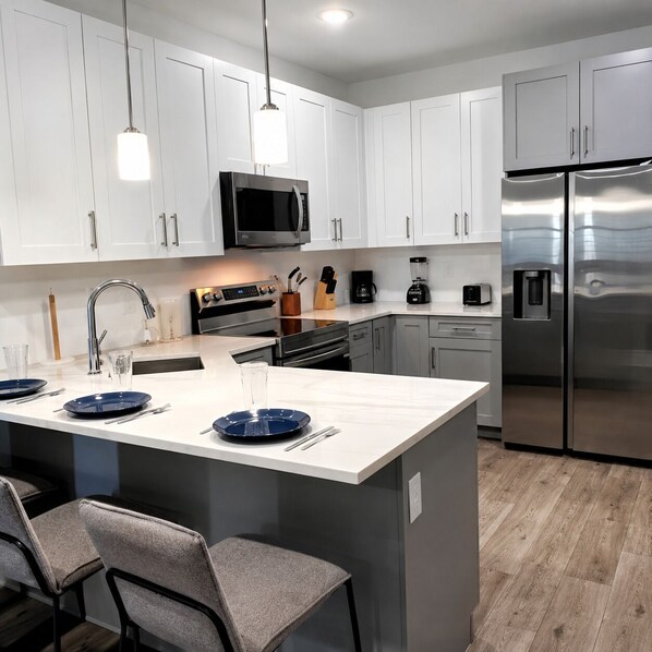 A modern kitchen with white cabinets, stainless steel appliances, a central island with blue plates, and a seating area with grey chairs.