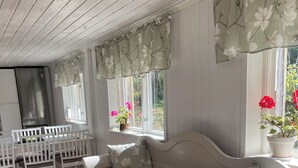 Een gezellige kamer met een witte bank, een eettafel met stoelen en een groot raam met gordijnen.