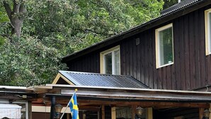 Een houten blokhut met veranda, vlag en een stenen muur.